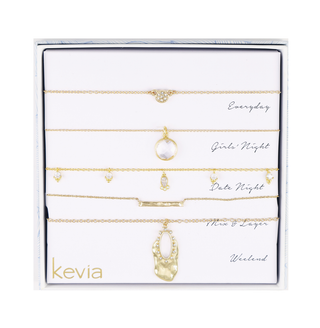 Five-piece gold necklace set with hammered gold accents, crystal drops, pavé charm, hammered bar, and sculptural drop pendant, packaged in a gift box.