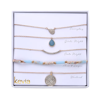 Layered necklace set with pavé teardrop pendant, gemstone charm, crystal bar, marbled beads, and a medallion pendant.