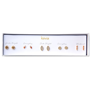Five-pair gold and orange earring set featuring knot studs, oval crystal studs, sparkly discs, and bar earrings with orange stones, packaged in a gift box