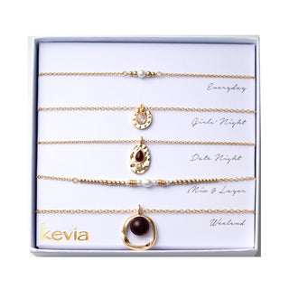 Five-piece gold necklace set with garnet stones, pearls, hammered gold pendants, and horseshoe charm, packaged in a gift box.