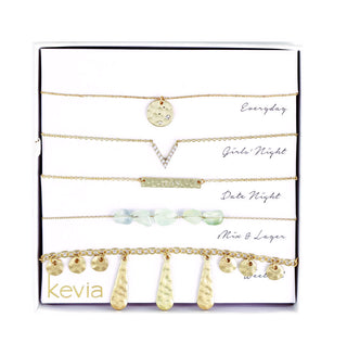 Five-piece gold necklace set featuring hammered gold pendants, sea glass beads, engraved "Joy" bar, and fringe accents, packaged in a gift box.