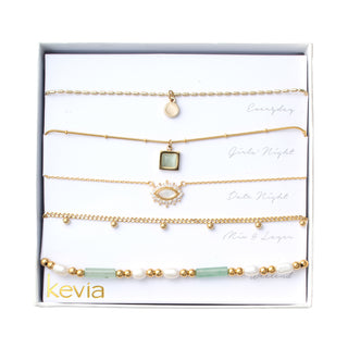 Five-piece gold-tone necklace set with seafoam and cream accents, including disc charm, gemstone pendant, pavé eye charm, bead chain, and pearl strand.