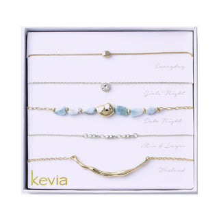 Five-piece necklace set in silver and gold tones with soft blue stones, sculptural metal accents, and a mix of chain styles, packaged in a white gift box.