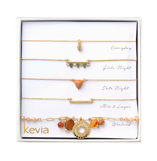 Five-piece gold necklace set with peach gemstones, marquise charm, crystal bar, and sunburst medallion, packaged in a gift box.