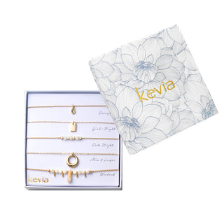 Five-piece gold necklace set with teardrop crystal pendant, gold rectangle charm, mother-of-pearl beads, circular gold pendant, and shell charm, packaged in a gift box.