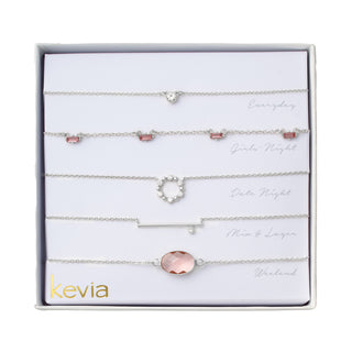 Five-piece silver necklace set with blush baguette charms, crystal circle, solitaire pendant, silver bar, and faceted blush gemstone.
