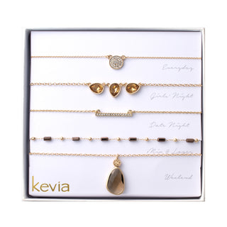 Five-piece gold necklace set with smoky quartz accents, pavé charm, crystal bar, and gemstone pendant, packaged in a gift box.