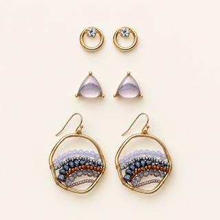 Three pairs of gold earrings with ombre bead circles, pale purple triangular stone studs, and small crystal-accented open circles on cream.