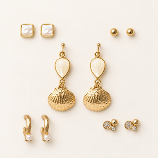 Five pairs of gold earrings with white pearl and textured shell drops, square iridescent studs, gold balls, crystal clusters, and small crystal drops on cream.