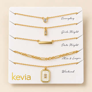 Five-piece gold necklace set on a Kevia card with crystal charms, slim bar, link chain, and rectangular mother-of-pearl pendant.