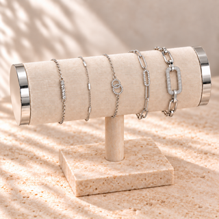 Five silver bracelets with crystal bar, rectangular stations, interlocking circles, elongated links, and pavé rectangular link on a cream display.