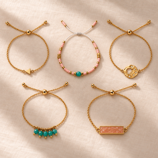 Five adjustable gold bracelets with coral rectangular stone, turquoise bead drops, pale pink beads, textured circle, and arrow charm on a cream surface.