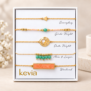 Five-piece gold bracelet set with coral rectangular stone, turquoise beads, pale pink beads, textured circle, and arrow charm in an open Kevia box.