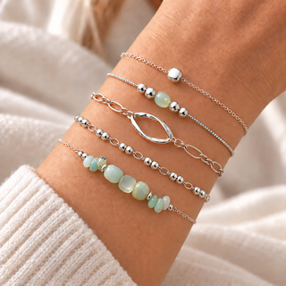 Close-up of a wrist wearing five silver bracelets with seafoam stone beads, silver beads, and an open oval link.