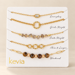 A jewelry gift set on a white display card labeled 'kevia', showing five gold-tone chain bracelets with different bead and charm designs and handwritten style labels: Everyday, Girls Night, Date Night, Mine & Layer, and Weekend.