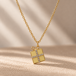 Gold chain necklace with a gift box pendant and crystal ribbon accents.