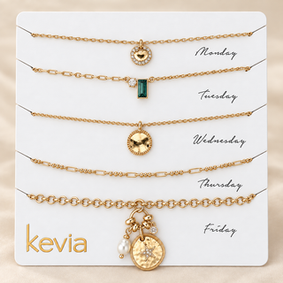 Five gold-toned chain necklaces with different pendant designs are displayed on a white card labeled Monday through Friday, with the brand name kevia at the bottom left.