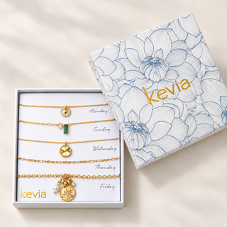 Five-piece gold necklace set with a green stone and star medallion in an open box beside a floral Kevia lid.