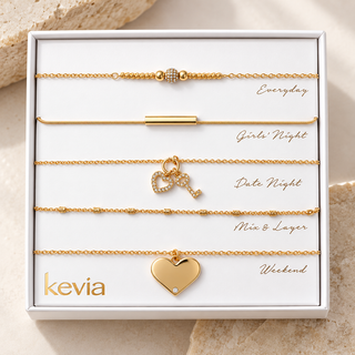 A boxed set of five gold-toned necklace layers displayed on a white insert card. The set includes Everyday, Girls' Night, Date Night, Mix & Layer, and Weekend styles, with one larger heart-shaped charm labeled Weekend.