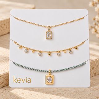 Three delicate gold and mint green necklaces displayed on a white branded card labeled 'kevia', set against a warm beige stone background.