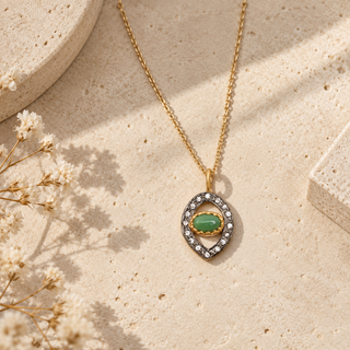 Gold chain necklace with a green oval stone in an open marquise crystal-bordered pendant.