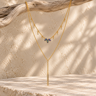 Gold layered necklace with an opal charm cluster and a long gold bar pendant.