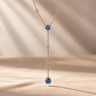 Close-up of a gold Y-shaped necklace with blue opals and small crystal accents.