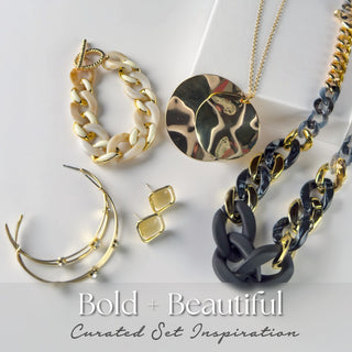 Bold and Beautiful five-piece mystery jewelry set featuring gold and black chain necklaces, chunky acetate bracelet, layered gold bangles, and geometric gold earrings. Packaged as a curated set inspiration.