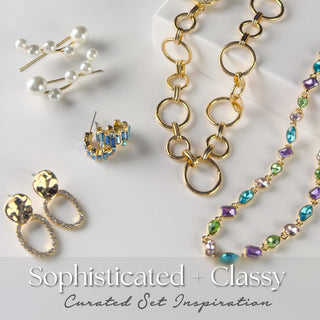 Sophisticated and Classy five-piece mystery jewelry set featuring pearl hairpins, faceted gold earrings, blue baguette hoops, oversized gold circle necklace, and a multicolor crystal strand. Packaged as a curated set inspiration.
