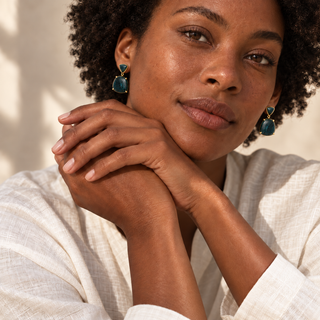 Model wearing gold drop earrings with deep green triangular tops and large rounded green stones.