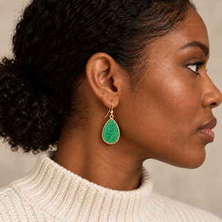 Model wearing a large green druzy teardrop earring in a gold setting.