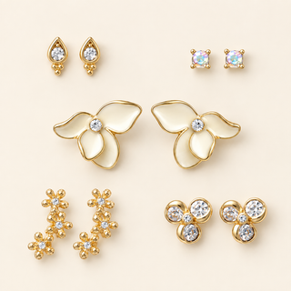 Five pairs of gold earrings with white enamel flowers, crystal teardrops, square studs, three-stone clusters, and floral climbers on cream.