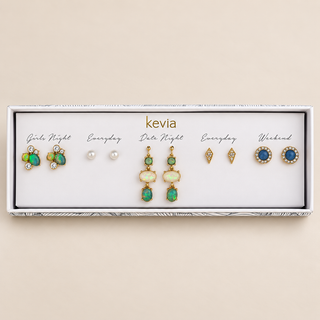 Five-pair gold earring set with green and opalescent drops, multicolor clusters, pearl studs, and blue crystal halos in an open Kevia box.
