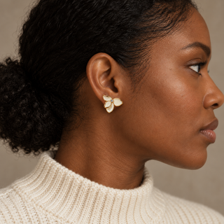 Model wearing a white enamel three-petal flower stud with a clear crystal center in a gold setting.