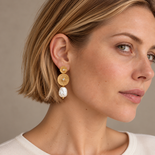 Model wearing a gold double-sunburst drop earring with a white baroque-style pearl.