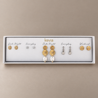 Five-pair mixed metal earring set with gold sunburst pearl drops, textured gold studs, clear studs, and silver pearl drops in an open Kevia box.