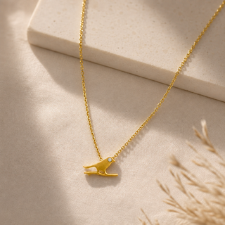 Gold chain necklace with a small bird pendant and a crystal accent.
