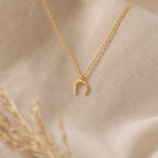 Gold chain necklace with a small horseshoe pendant.