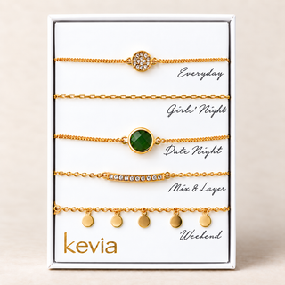 Five-piece gold bracelet set with a green round stone, pavé circle, crystal bar, fine chain, and disc drops in an open Kevia box.