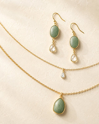 Jewelry set with gold necklaces and earrings featuring green gemstones on a beige background