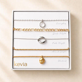 A boxed set of five delicate chain necklaces in silver and gold tones, arranged on a white insert card labeled with different lifestyle scenarios (Everyday, Date Night, etc.) and the brand name 'kevia' at the bottom left.