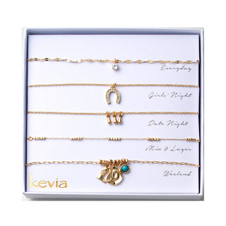 Five-piece gold necklace set with crystal pendant, pavé horseshoe charm, boot charms, textured layering chain, and turquoise cowboy hat charm, packaged in a gift box.