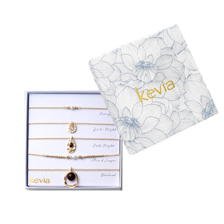 Five-piece gold necklace set with garnet stones, pearls, hammered gold pendants, and horseshoe charm, packaged in a gift box.