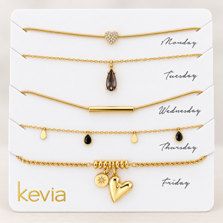 A jewelry display card showing five gold-toned necklaces labeled Monday through Friday, with the brand name kevia in gold at the bottom left. The necklaces include a heart charm, teardrop charms, a bar charm, and small dangling charms on a white card.