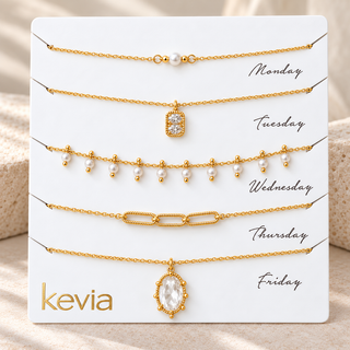 Five gold-toned chain necklaces displayed on a white card labeled Monday through Friday, with the brand name kevia at the bottom left. The necklaces feature different designs including a small rectangular pendant, pearl drops, a link chain, and an oval pendant.