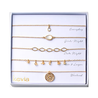 Five-piece gold necklace set with crystal teardrop pendant, mother-of-pearl oval station, open-link chain, golden chip-stone charms, and sunburst medallion, packaged in a gift box.