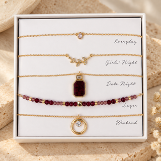 Five-piece gold necklace set with a red stone pendant, garnet beads, crystal leaf detail, solitaire, and open circle in an open Kevia box.