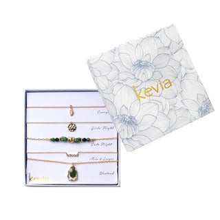 Five-piece necklace set featuring a fine chain necklace with a small bezel-set clear crystal pendant, a hammered disc pendant necklace, a green stone beaded necklace with gold spacer accents, a slim crystal station chain necklace, and a faceted green stone pendant necklace framed in an organic gold setting, packaged in a gift box.