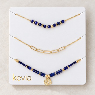 Three gold-tone beaded and chain necklaces displayed on a white Kevia jewelry card against a light beige background.
