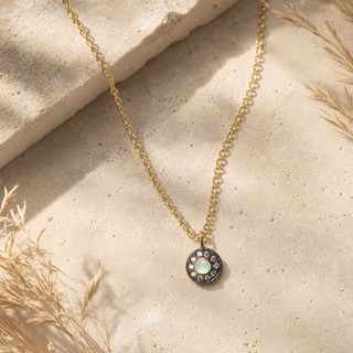 Gold chain necklace with a round pale green stone pendant and a dark crystal halo.